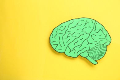 Photo of Paper cutout of human brain on yellow background, top view. Space for text