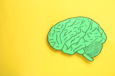 Paper cutout of human brain on yellow background, top view. Space for text