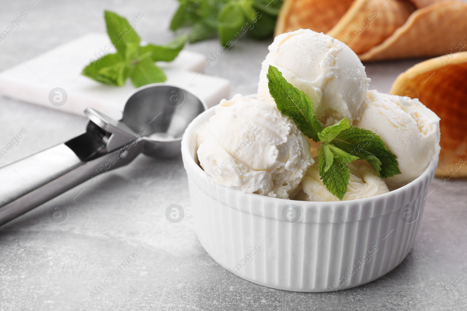Photo of Delicious vanilla ice cream with mint and scoop on light grey table, closeup. Space for text