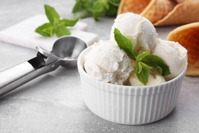 Delicious vanilla ice cream with mint and scoop on light grey table, closeup. Space for text