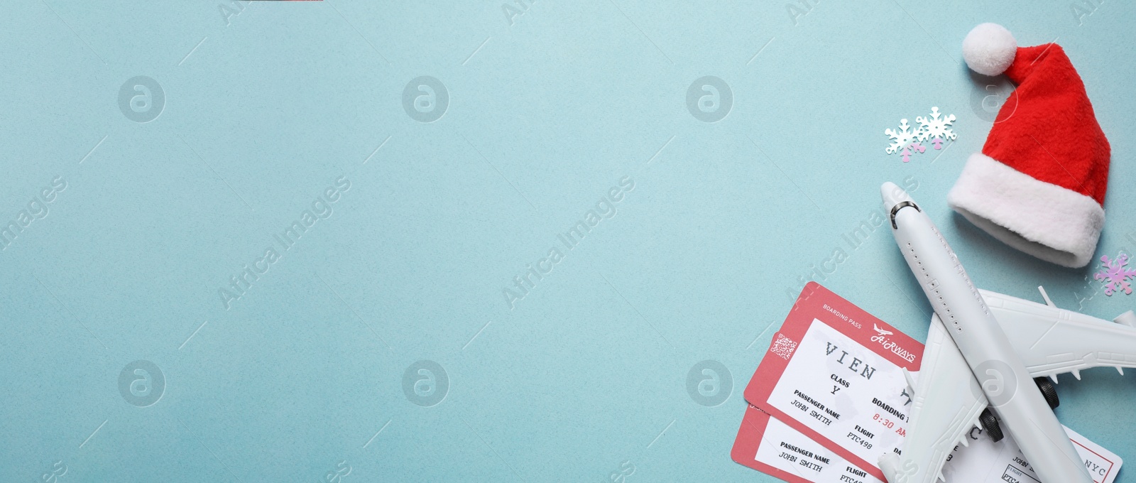 Image of Santa hat, toy airplane and airline tickets on light blue background, space for text. Christmas vacation