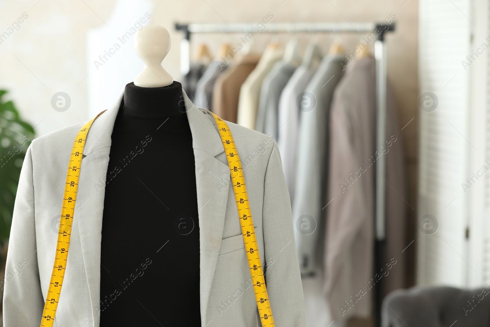 Photo of Mannequin with jacket and measuring tape in tailor shop, space for text