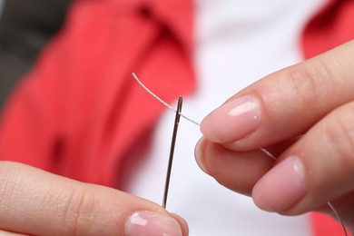 Photo of Woman inserting thread through eye of needle, closeup