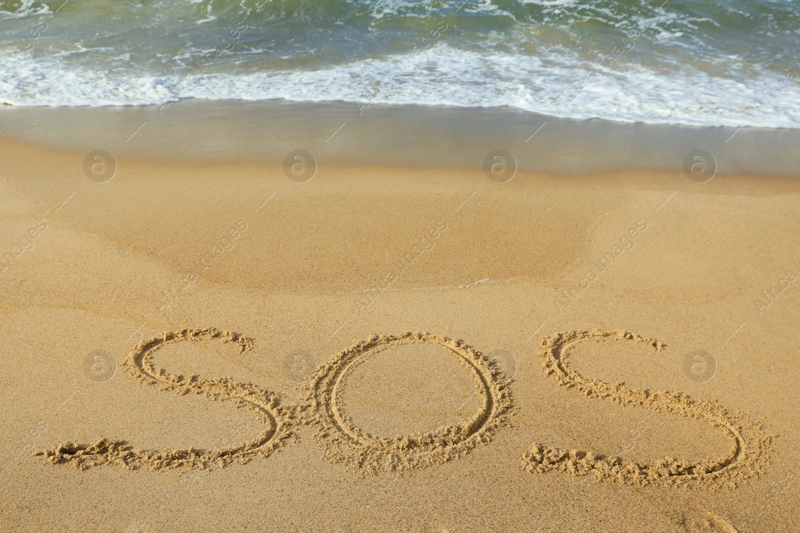 Photo of Message SOS drawn on sand near wavy sea