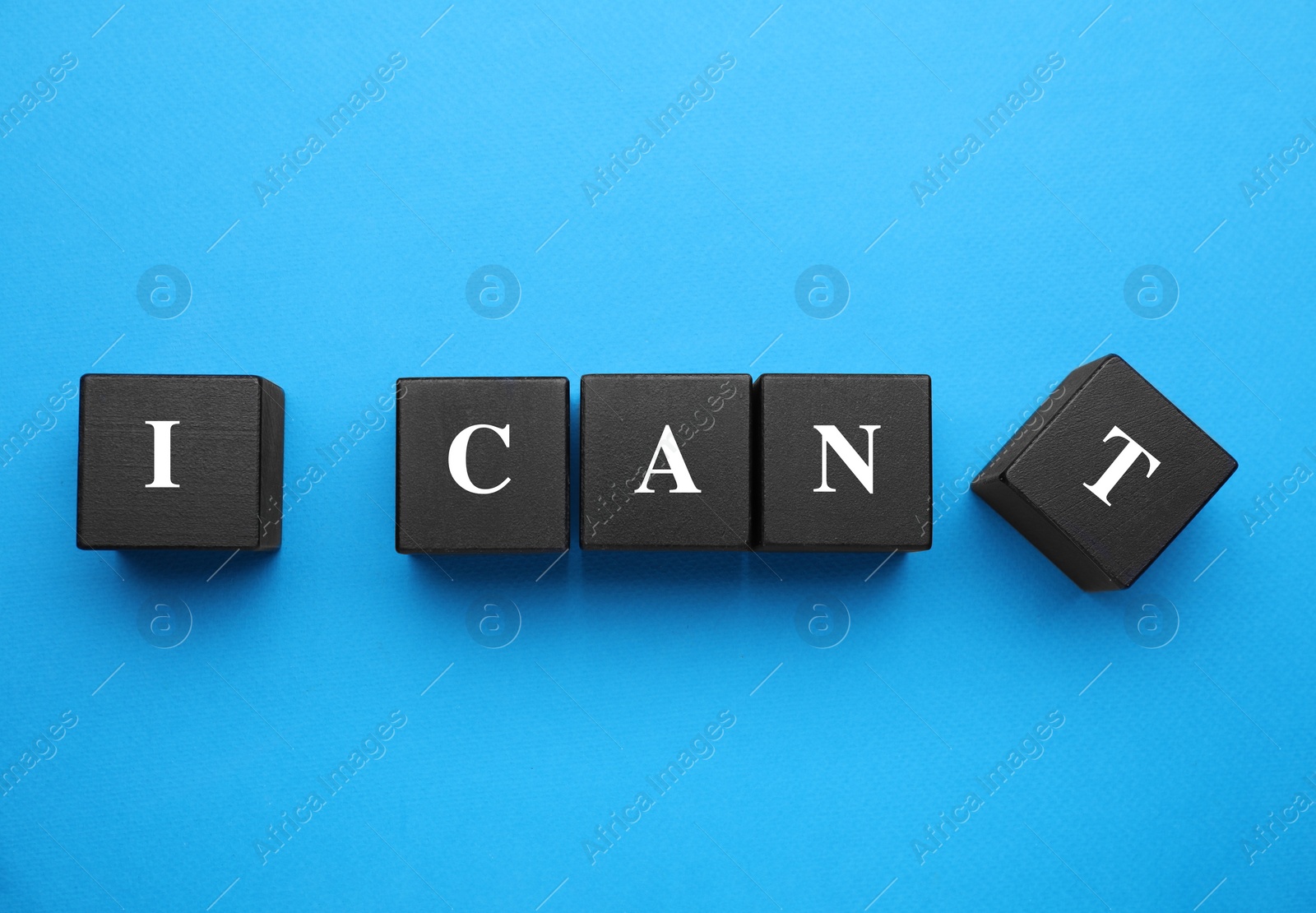 Photo of Motivation concept. Changing phrase from I Can't into I Can by removing black wooden cube with letter T on light blue background, flat lay