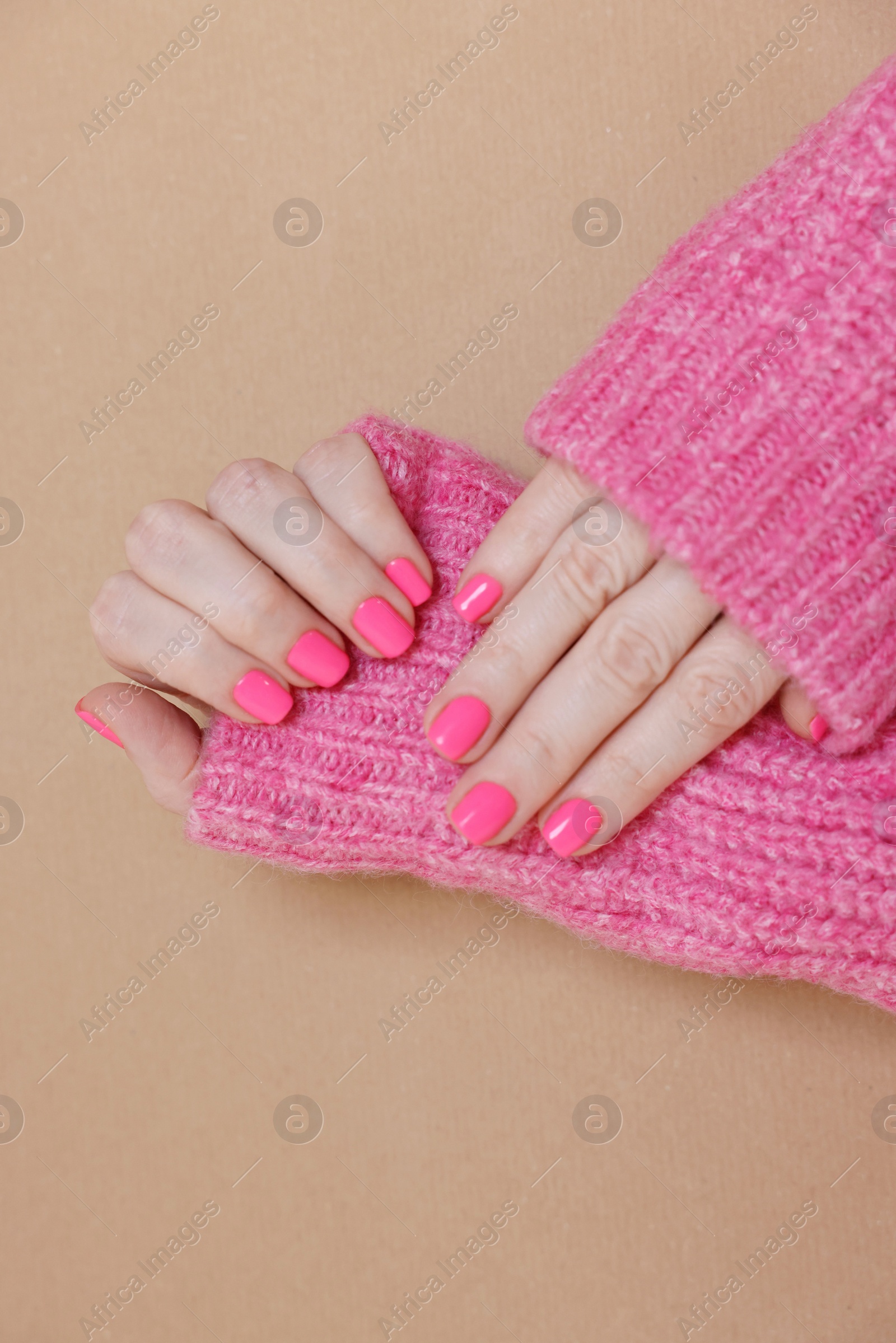 Photo of Woman showing her manicured hands with pink nail polish on dark beige background, closeup