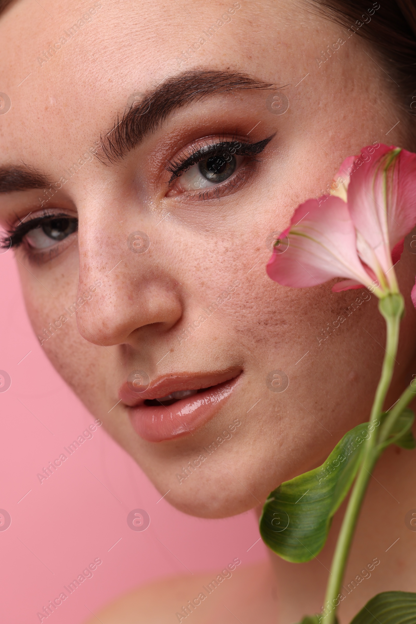 Photo of Beautiful woman with fake freckles and flower on pink background, closeup