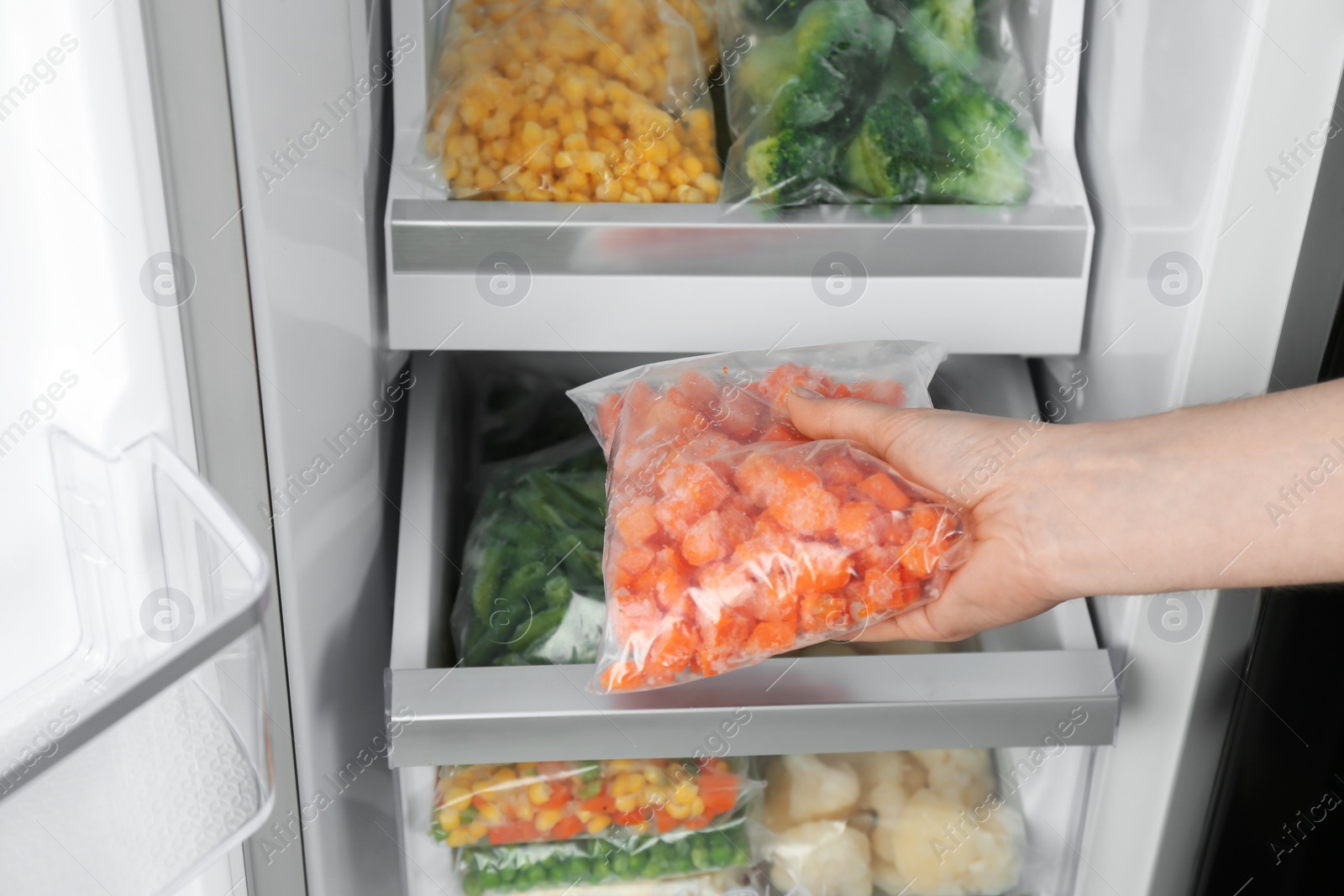 Photo of Woman taking plastic bag with frozen carrot from refrigerator, closeup