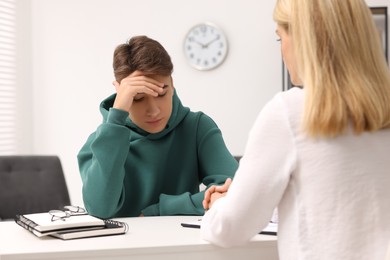 Psychologist working with teenage boy at table in office