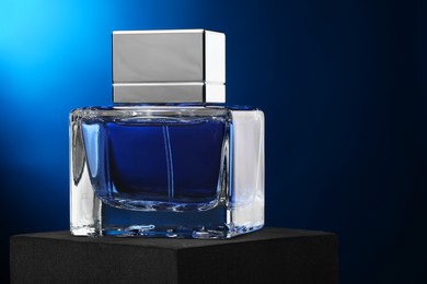 Photo of Luxury men`s perfume in bottle against dark blue background, space for text