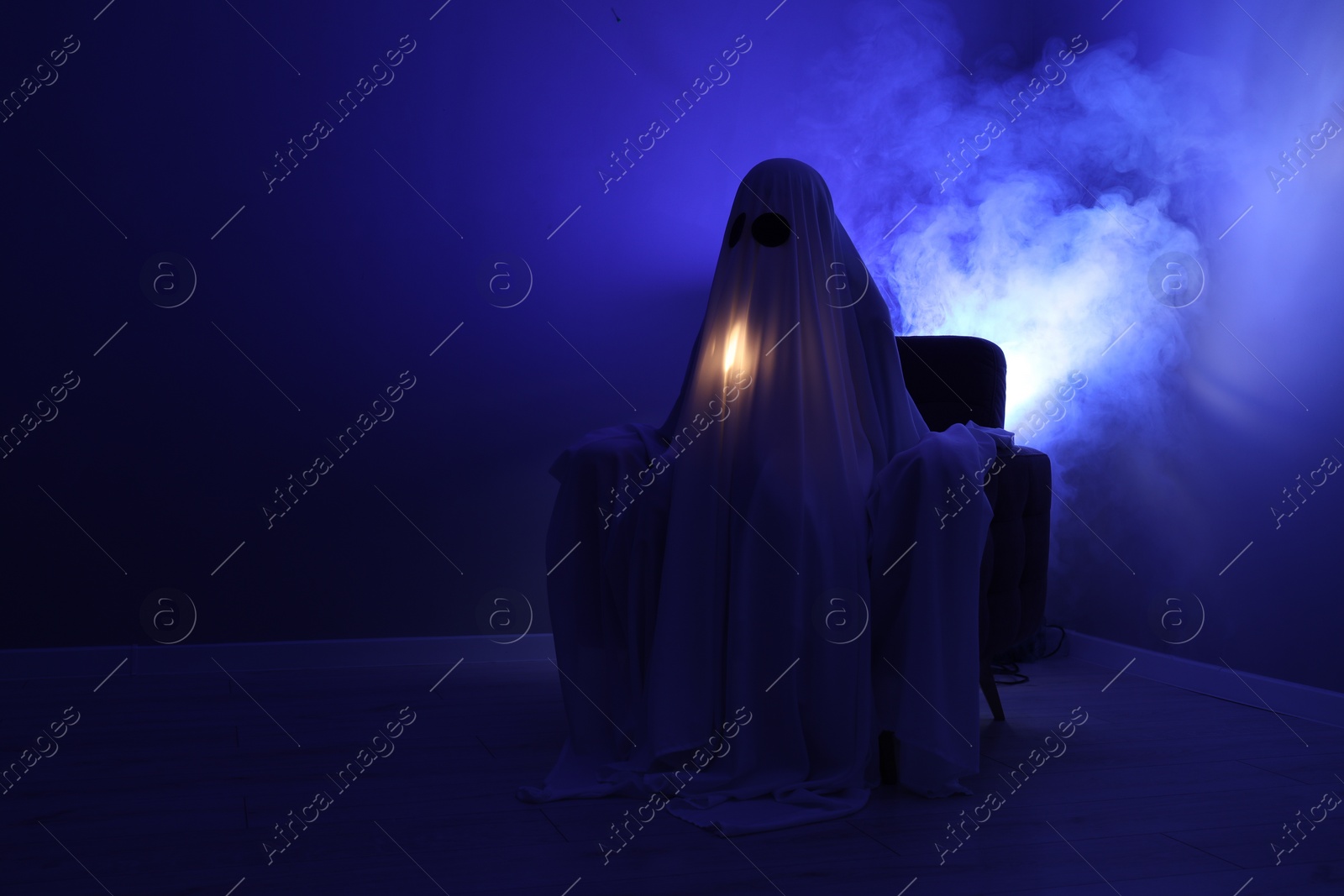 Photo of Creepy ghost. Woman covered with sheet sitting in armchair in blue light, space for text