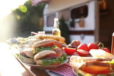 Photo of Delicious burgers on wooden table outdoors. Camping season