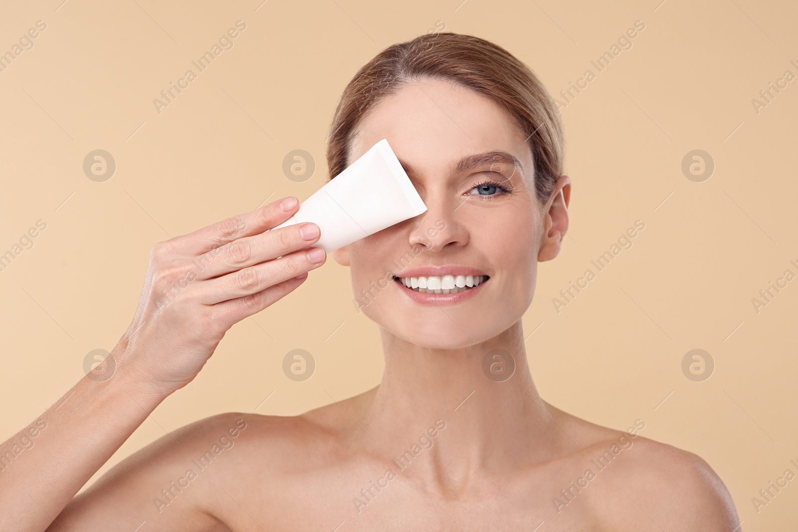 Photo of Woman holding tube of foundation on beige background