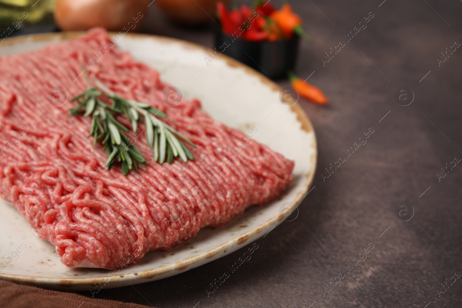 Photo of Fresh raw ground meat and rosemary on brown textured table, closeup. Space for text