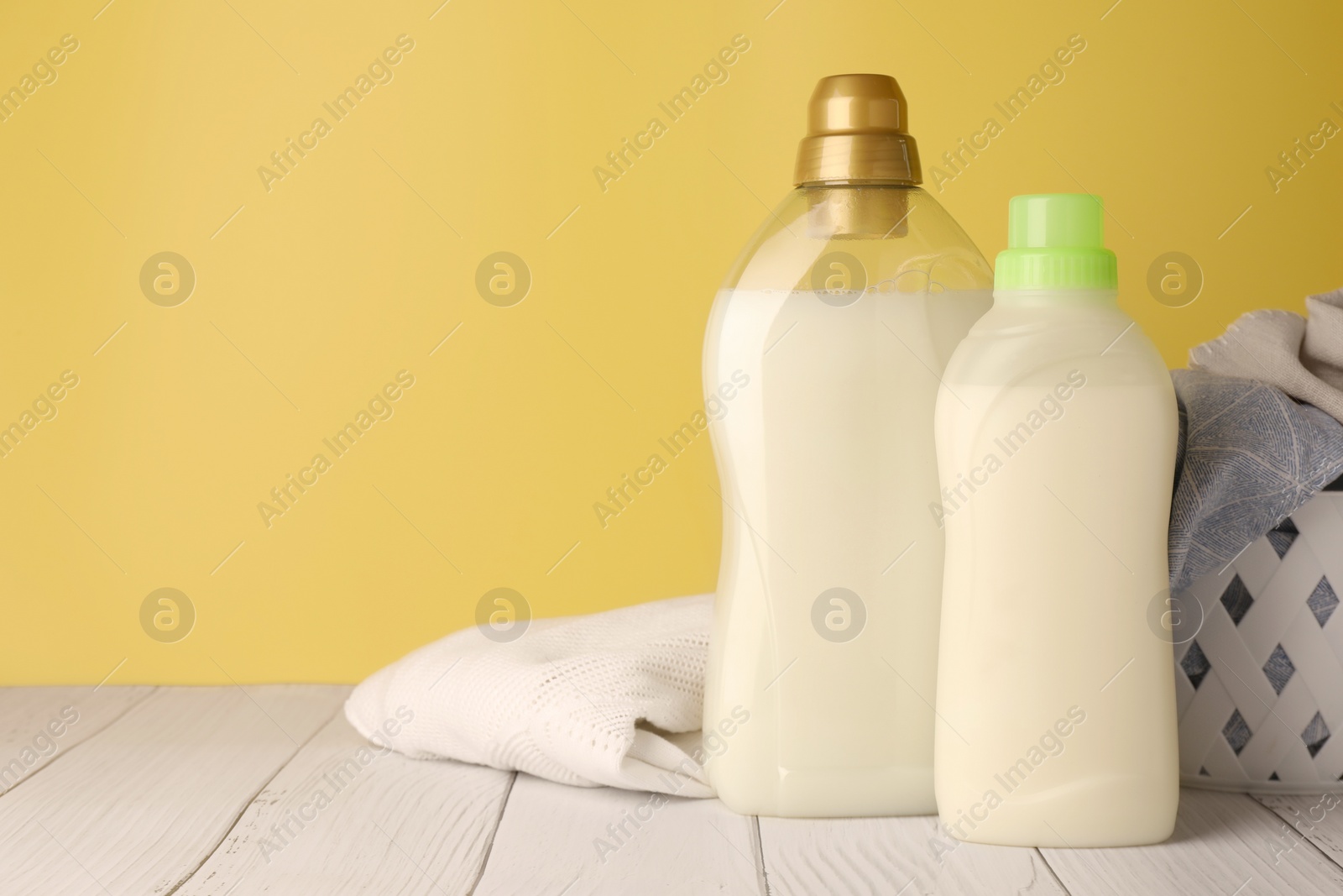 Photo of Bottles of fabric softener and clothes on white wooden table, space for text