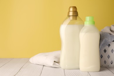 Photo of Bottles of fabric softener and clothes on white wooden table, space for text