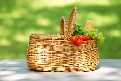Photo of Wicker basket with food on table in park. Summer picnic