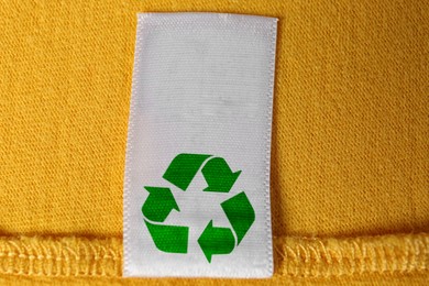 Clothing label with recycling symbol on yellow sweater, closeup view