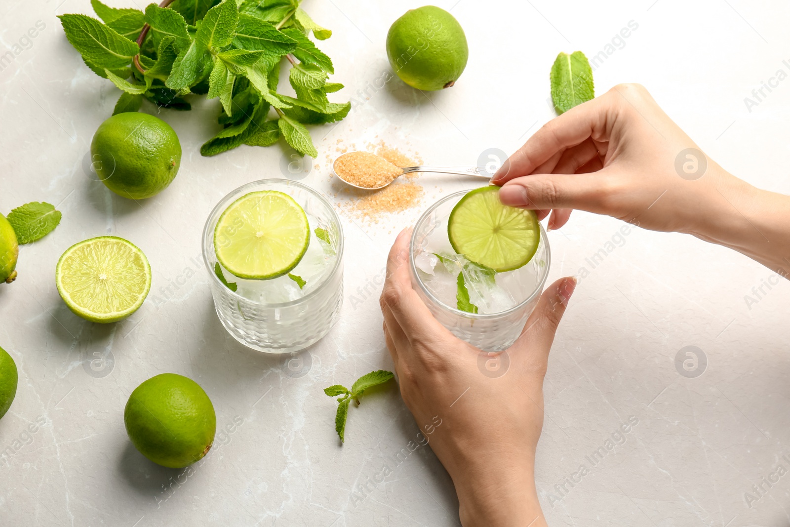 Photo of Young woman making delicious mint julep cocktail at table