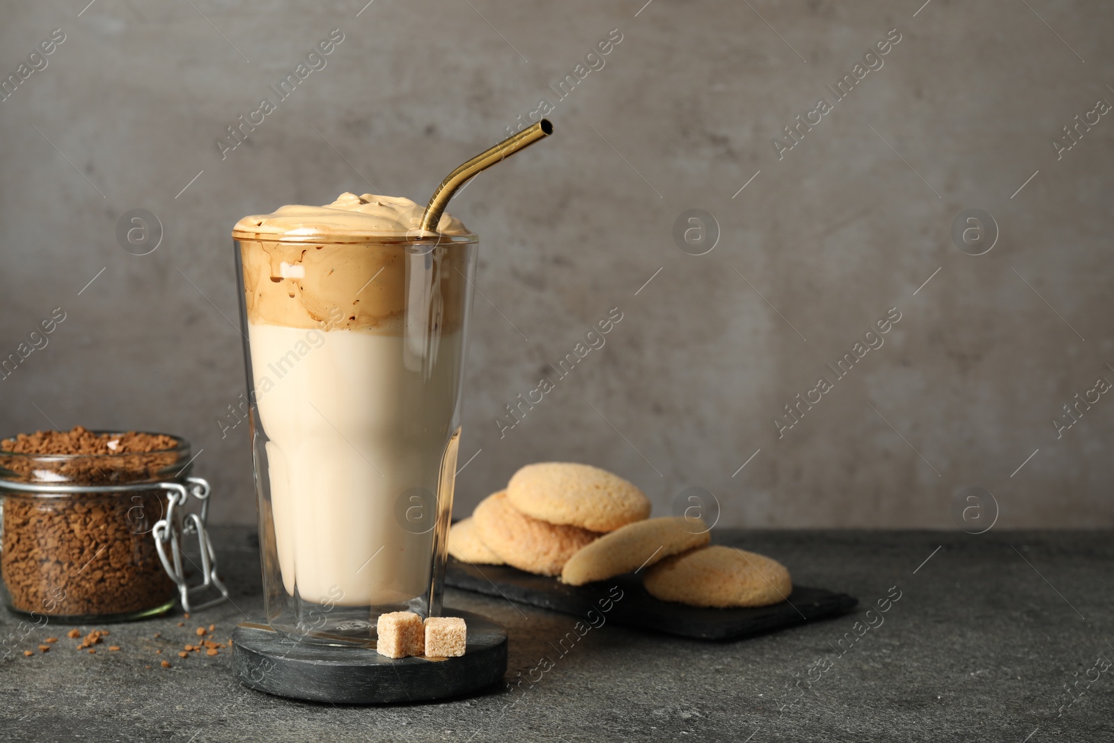 Photo of Glass of delicious dalgona coffee and cookies on grey textured table. Space for text