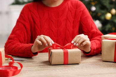 Photo of Woman with Christmas gift box at wooden table indoors, closeup