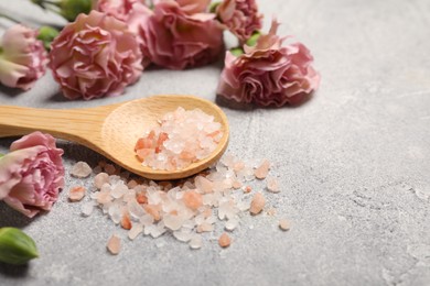 Wooden spoon with natural sea salt and beautiful flowers on light grey table