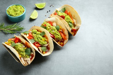 Delicious tacos with guacamole, meat and vegetables on grey table. Space for text