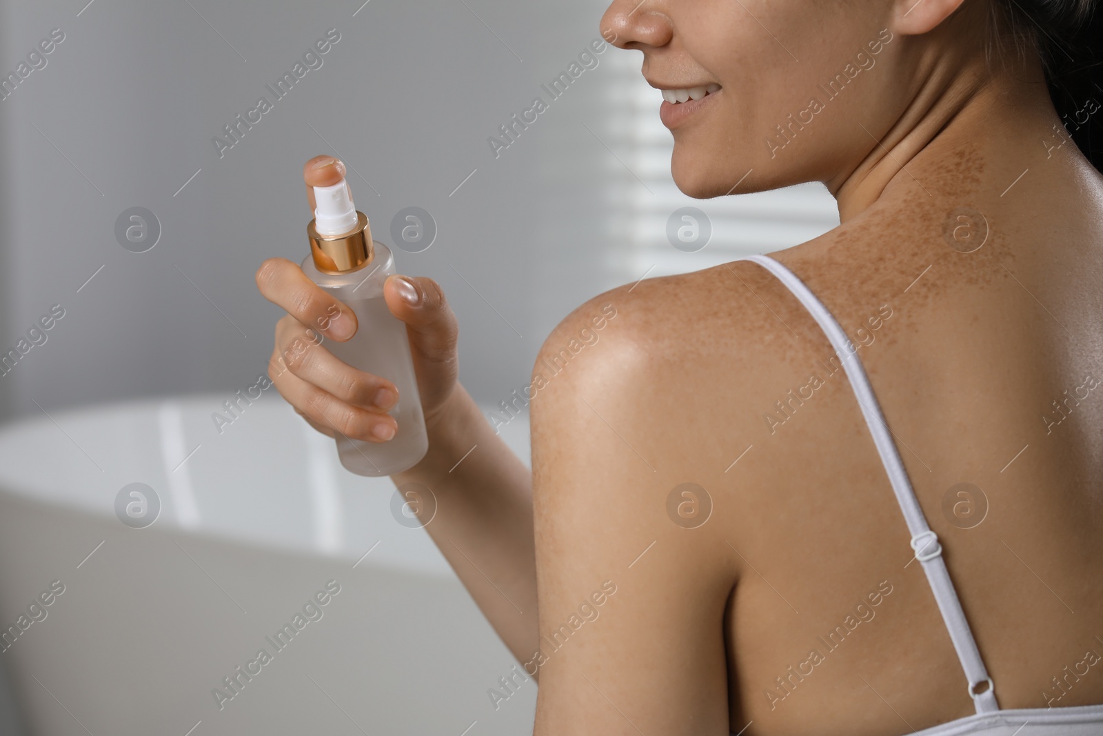 Photo of Young woman holding bottle of body oil in bathroom, closeup. Space for text