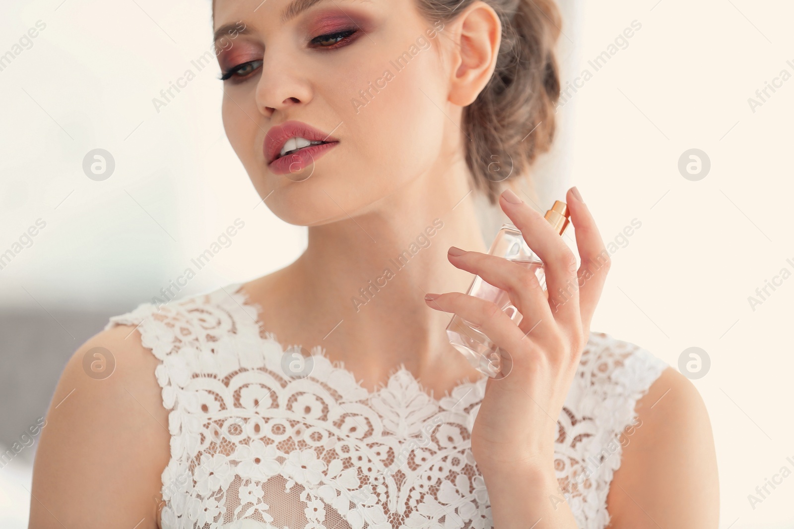 Image of Beautiful young bride with bottle of perfume on blurred background, closeup
