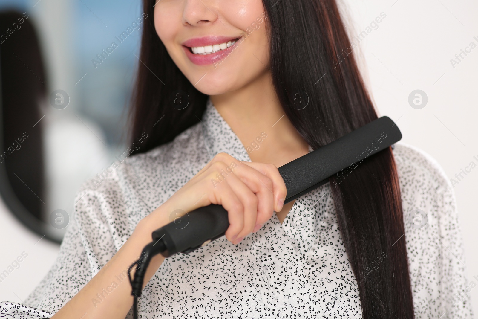 Photo of Happy woman using hair iron indoors, closeup