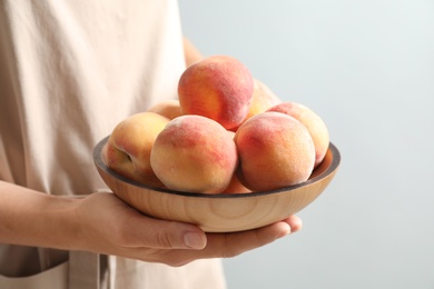 Photo of Woman holding plate with fresh sweet peaches, closeup