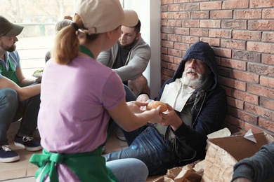 Photo of Volunteer giving food to poor senior man indoors