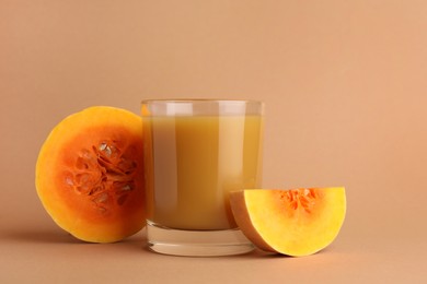 Tasty pumpkin juice in glass and cut pumpkin on pale orange background