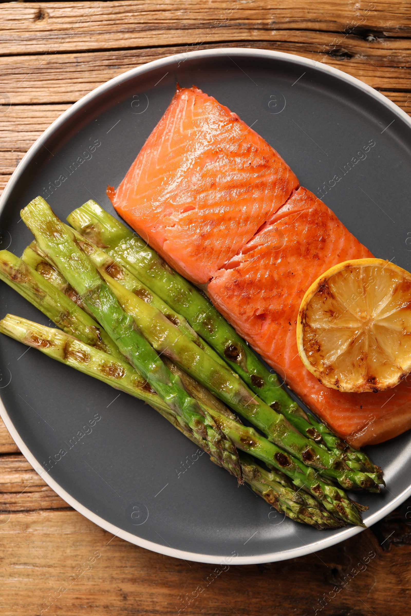 Photo of Tasty grilled salmon with asparagus and lemon on wooden table, top view