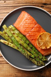 Photo of Tasty grilled salmon with asparagus and lemon on wooden table, top view