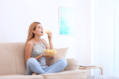 Photo of Woman with bowl of potato chips sitting on sofa in living room. Space for text