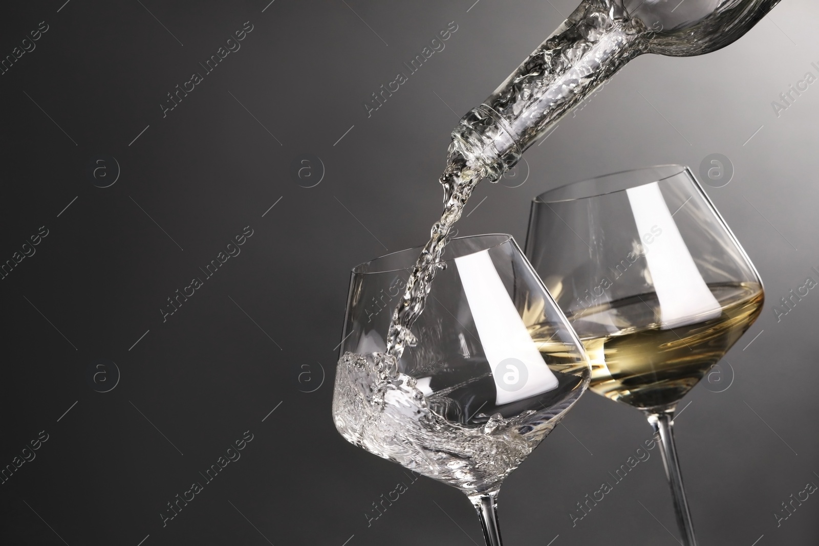 Photo of Pouring white wine into glass against grey background, closeup. Space for text