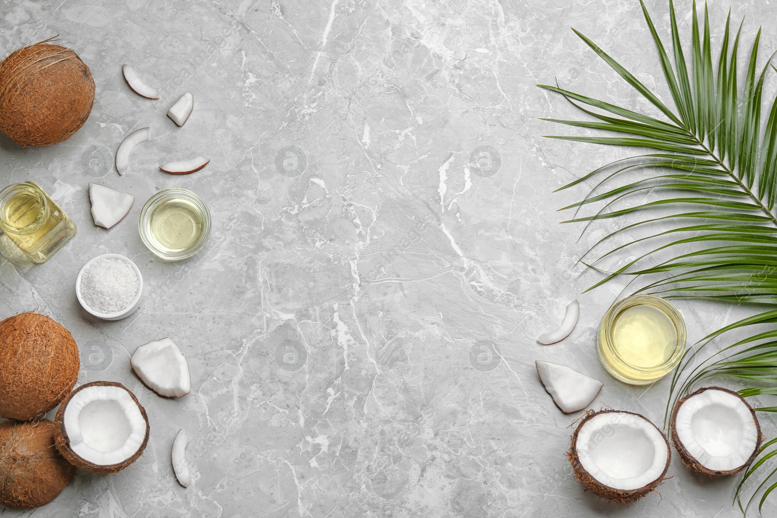 Photo of Glassware with natural organic oil and coconuts on grey stone background, flat lay. Space for text