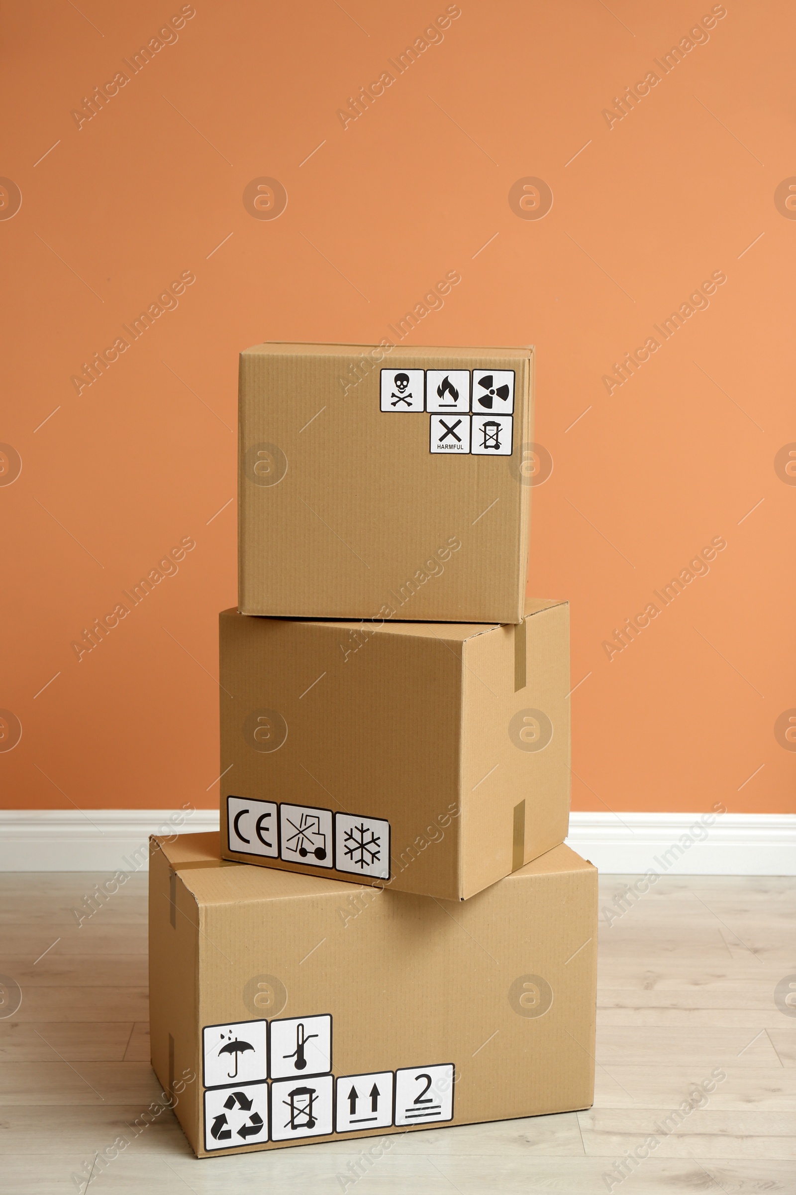 Photo of Cardboard boxes with different packaging symbols on floor near orange wall. Parcel delivery