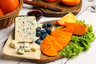 Delicious persimmon, blue cheese and blueberries served on white wooden table