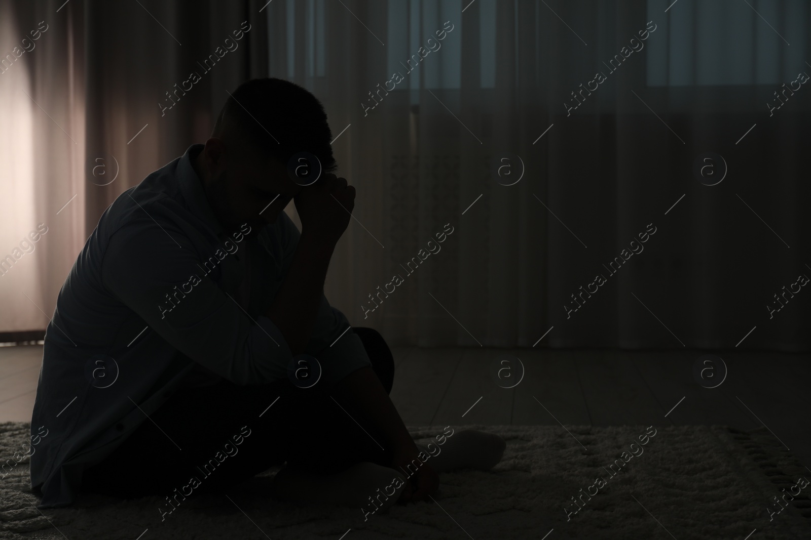 Photo of Silhouette of sad man in dark room. Space for text