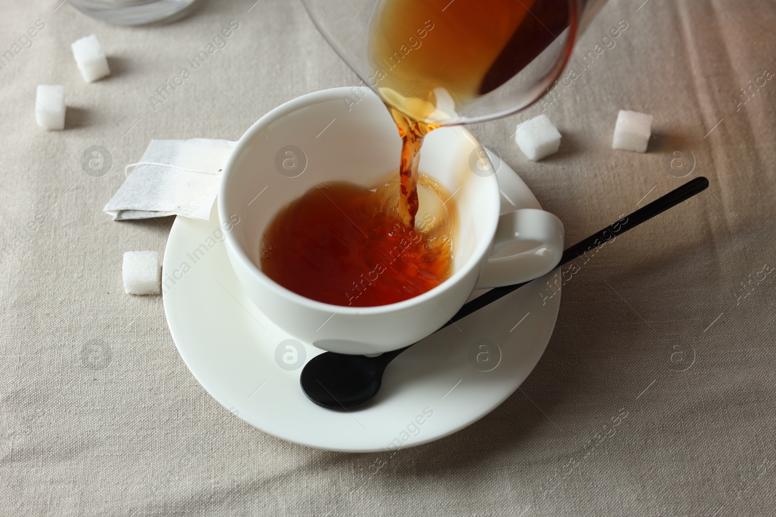 Photo of Pouring warm tea into cup on light table, closeup