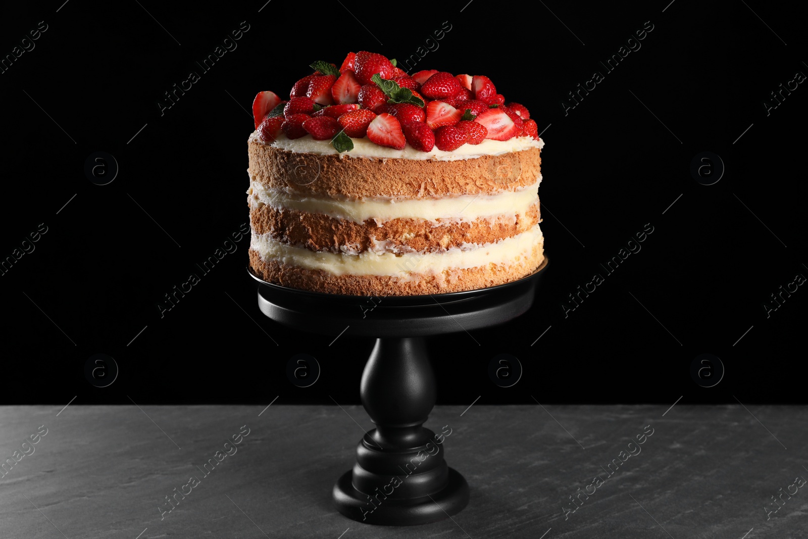 Photo of Tasty cake with fresh strawberries and mint on dark gray table against black background