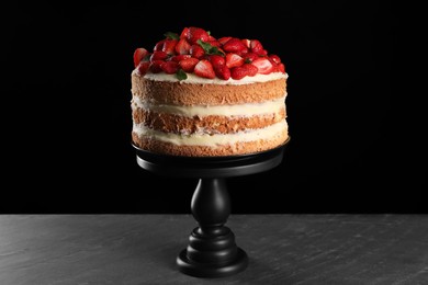 Tasty cake with fresh strawberries and mint on dark gray table against black background