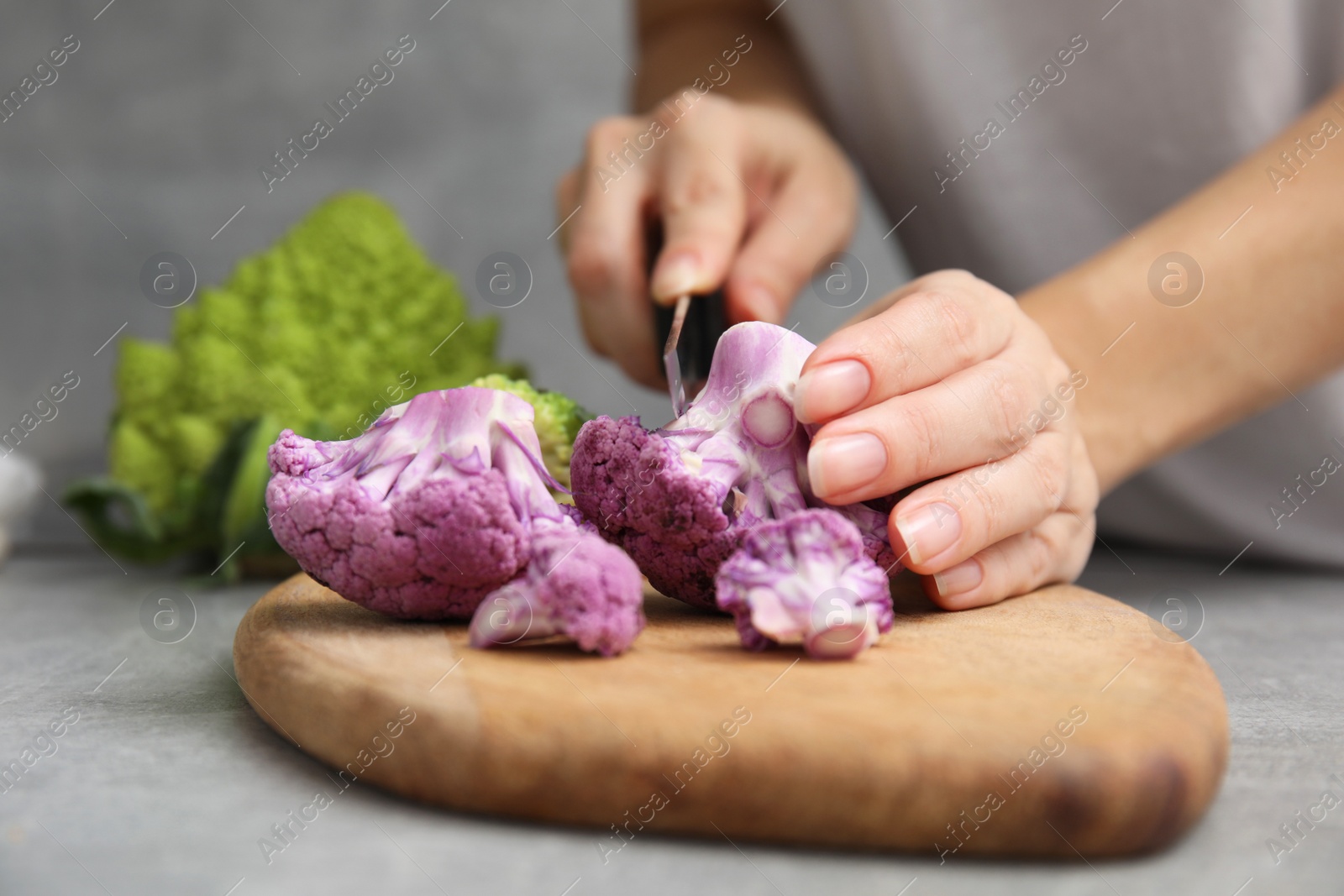 Photo of Woman cutting fresh purple cauliflower at grey table, closeup