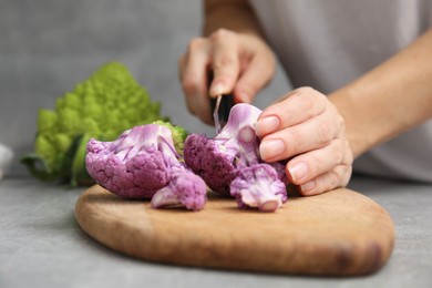 Photo of Woman cutting fresh purple cauliflower at grey table, closeup