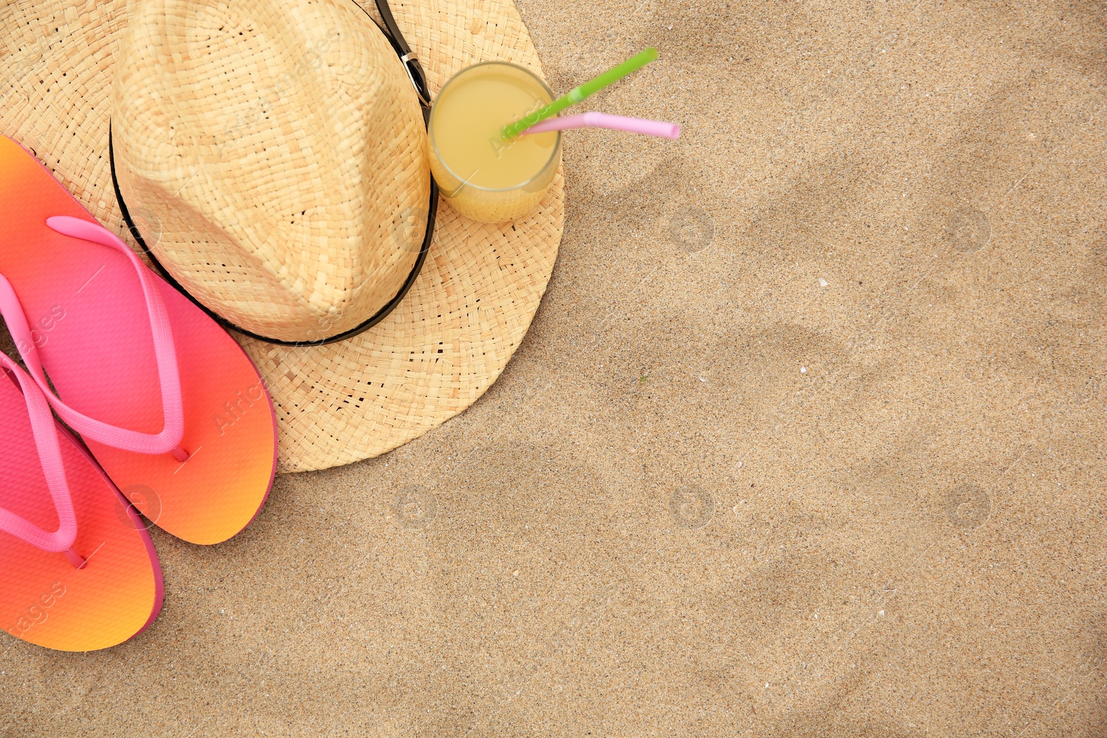 Photo of Straw hat, flip flops and refreshing drink on sand, flat lay with space for text. Beach accessories