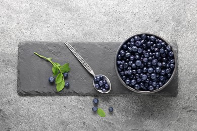 Tasty fresh bilberries and green leaves on grey table, flat lay