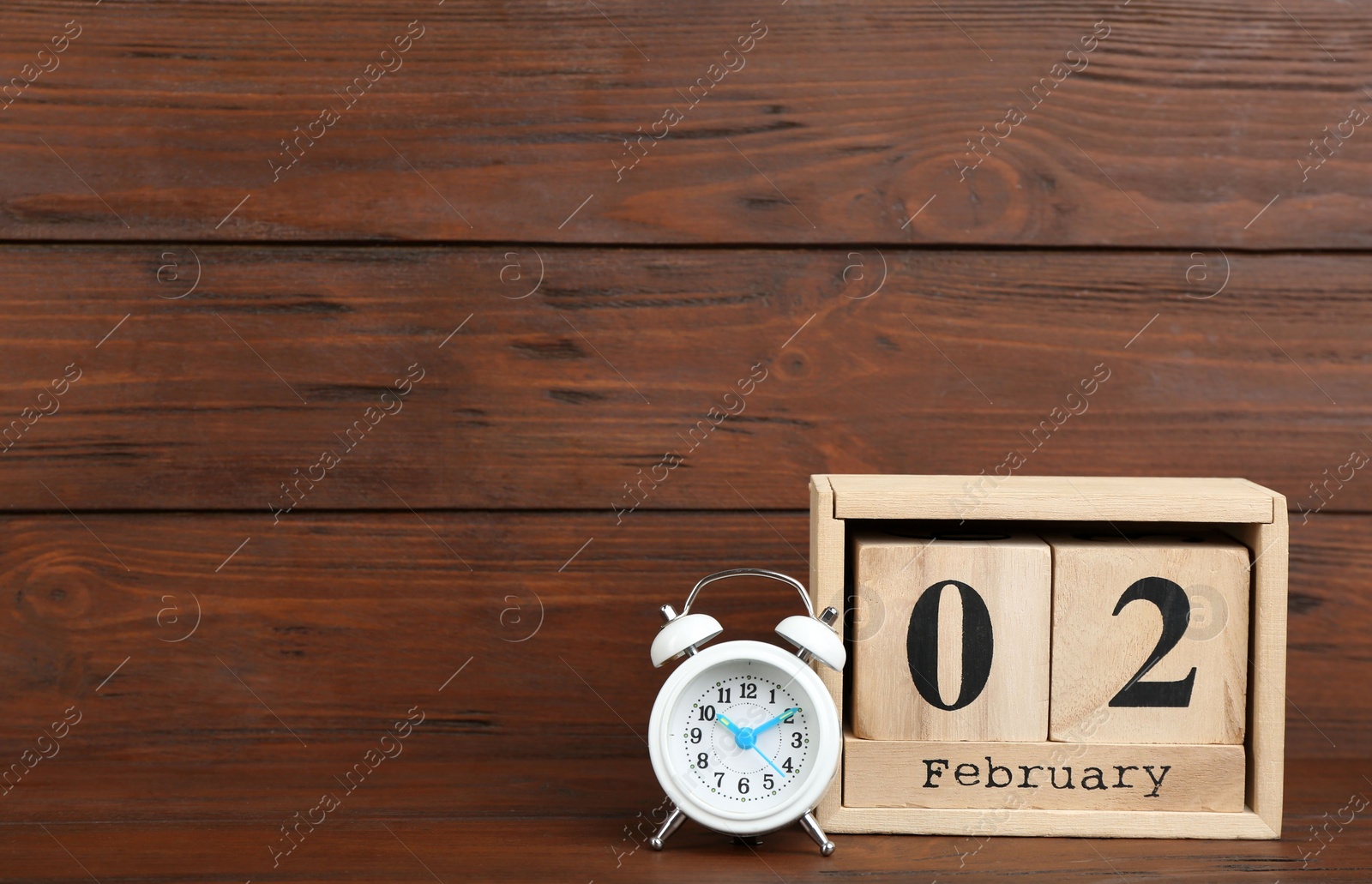 Photo of Wooden block calendar and alarm clock on table. Space for text