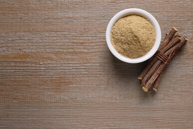 Powder in bowl and dried sticks of liquorice root on wooden table, flat lay. Space for text